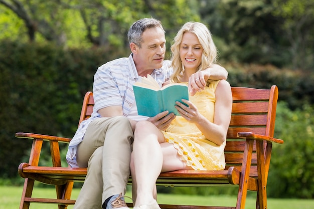 Casal feliz lendo um livro no banco do lado de fora