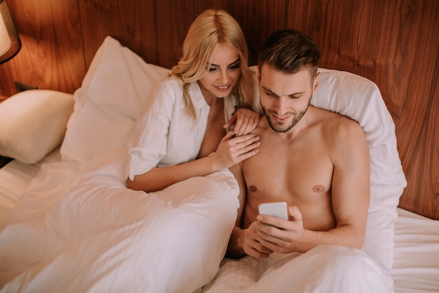 Casal feliz na cama e usar telefone celular