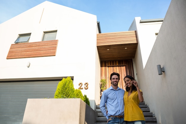 Casal feliz na frente da casa nova mostrando chaves