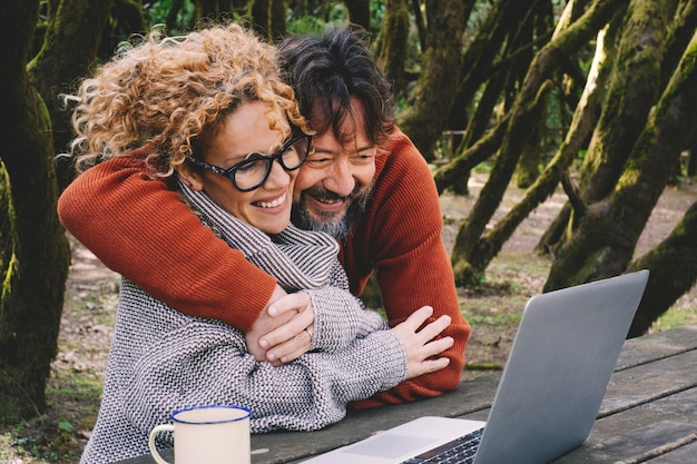 Casal feliz no amor e na amizade desfruta de videochamada no laptop juntos abraçando e sorrindo Natureza ao ar livre fundo da floresta Conceito de usar computador em todos os lugares Viaje pessoas de aventura moderna