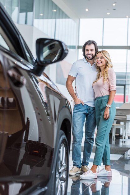 casal feliz olhando para um novo automóvel no salão de concessionários