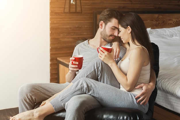 Casal feliz, passando a manhã juntos. mulher sentada no colo do homem, amando a família, bebendo café e se abraçando, copie o espaço