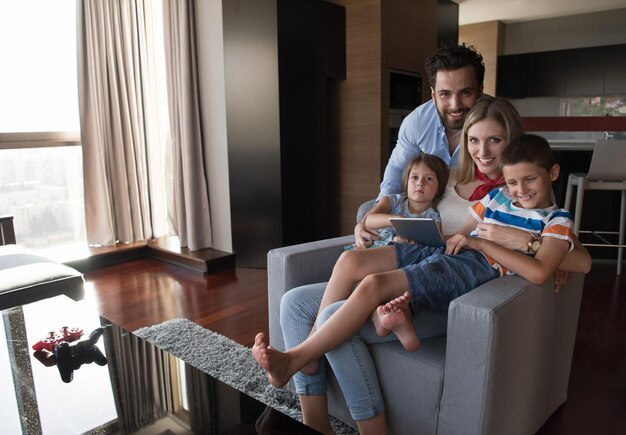 Foto casal feliz passando tempo com crianças usando computador tablet em uma poltrona em casa