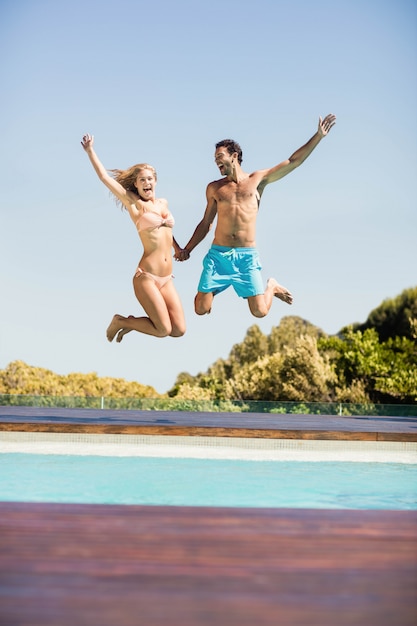 Casal feliz pulando na piscina em um dia ensolarado