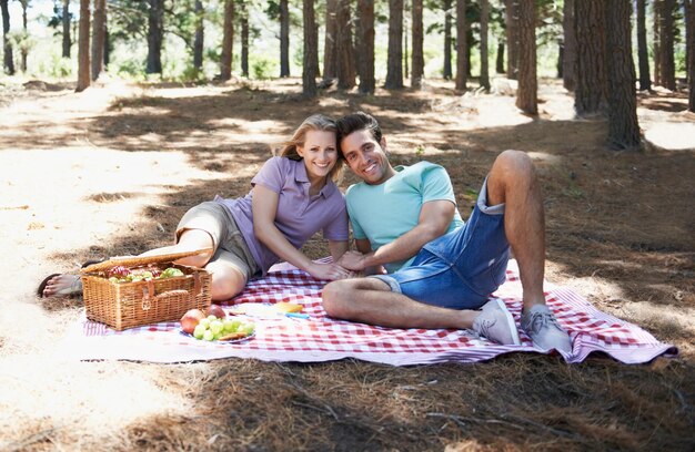 Foto casal feliz retrato de piquenique e natureza com amor celebração romântica e data de verão para o dia de são valentim jovens com comida frutas e relaxar em cobertor na floresta ou floresta para o aniversário