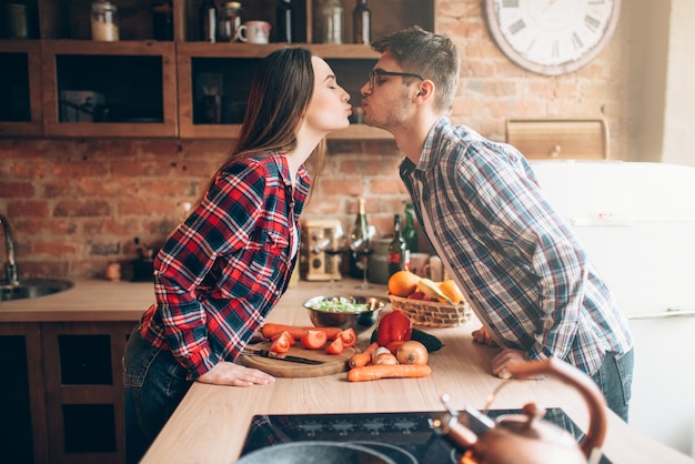 Casal feliz se beijando enquanto preparava um jantar romântico. Preparação de salada de legumes. Família prepara comida saudável na cozinha