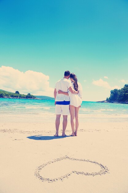 casal feliz se diverte e relaxa no verão com desenho de coração na areia da praia