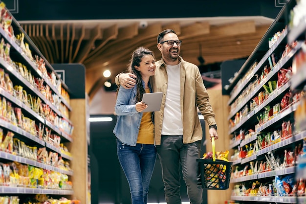 Casal feliz seguindo a lista no tablet e compras no supermercado