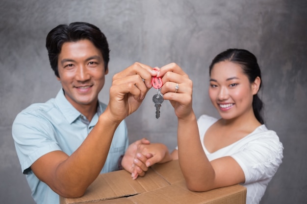 Casal feliz segurando a chave da casa e apoiando-se na caixa em movimento