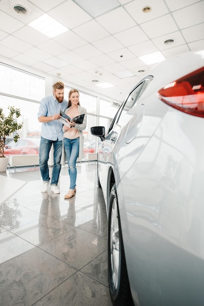 Casal feliz segurando catálogo e escolhendo carro no salão da concessionária
