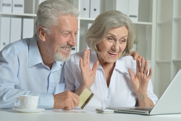 Casal feliz sênior com laptop e cartão de visita em casa