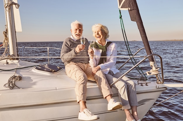 Casal feliz sênior sentado ao lado do barco a vela ou do convés do iate flutuando no mar, homem e mulher