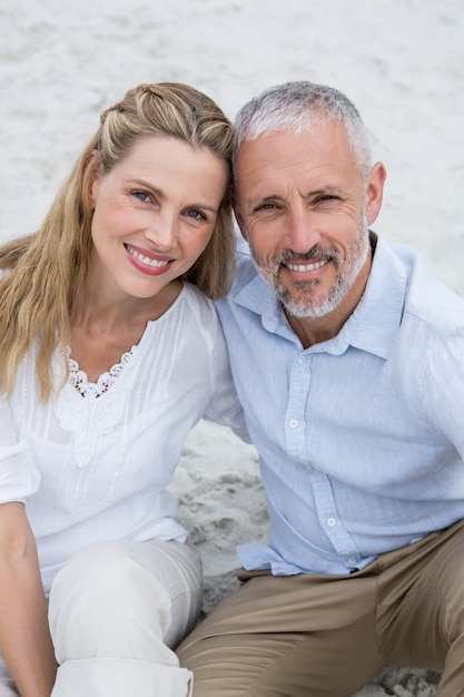 Foto casal feliz sentado na areia e olhando a câmera