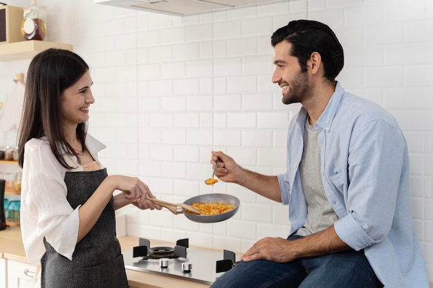 Foto casal feliz sentado na cozinha comendo espaguete rindo com esposa feliz e hashband comendo massas em cozinha de cores claras jantar romântico em casa juntos