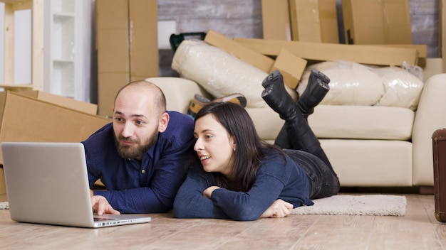 Casal feliz sentado no chão de seu novo apartamento enquanto fazia compras online no laptop. Amplie a imagem.