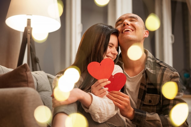 Foto casal feliz sentado no sofá nos braços de um coração vermelho. bokeh bonito turva. conceito romântico.