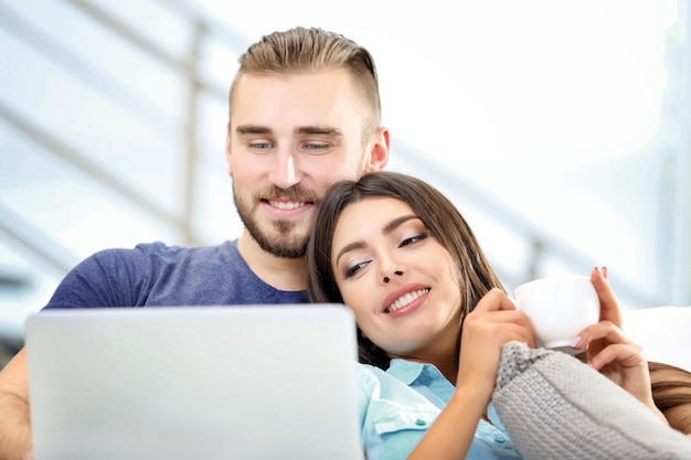 Casal feliz sentado no sofá tomando café e trabalhando em um laptop