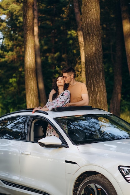 Casal feliz sentado no topo do telhado da minivan ao pôr do sol Jovens se divertindo nas férias de primavera viajando ao redor do mundo Travellove e conceito de férias Foco nos rostos