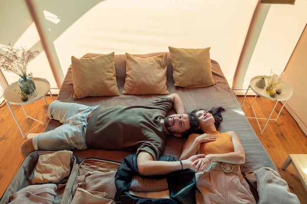 Foto casal feliz sonhando acordado deitado na cama com as malas desempacotadas