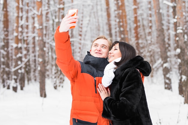 casal feliz tirando foto com smartphone sobre fundo de inverno.