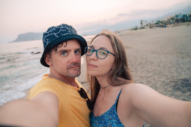 Foto casal feliz tirando uma foto em uma praia no mar na cidade de alanya, turquia, viajando ou de férias