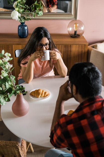 Casal feliz tomando café da manhã e conversando na mesa de jantar na manhã, garota indiana e cara latino rela