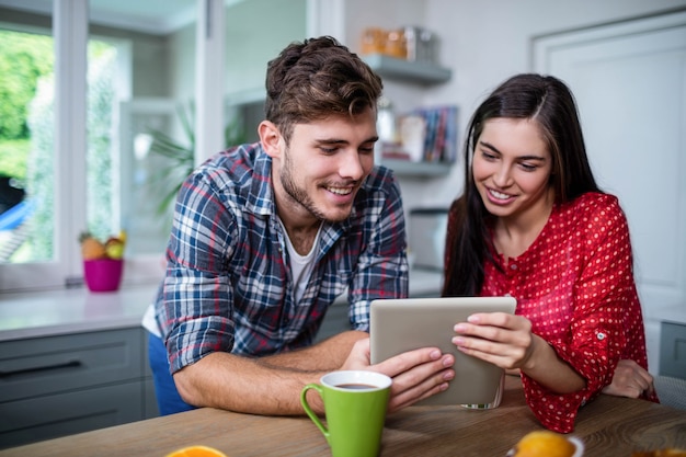 Casal feliz tomando café da manhã e usando o tablet em casa