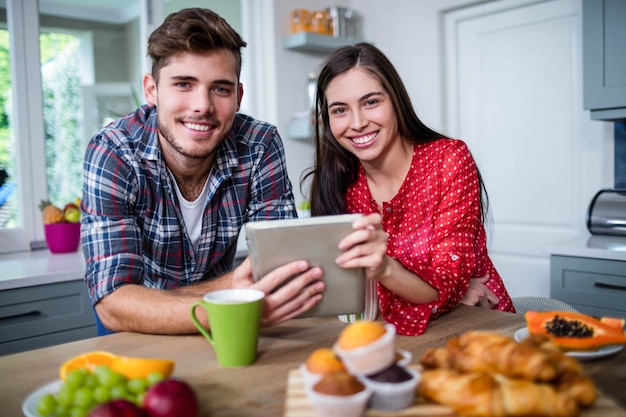 Casal feliz tomando café da manhã e usando o tablet em casa