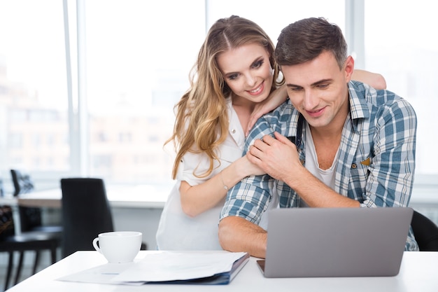 Casal feliz tomando café e usando laptop juntos