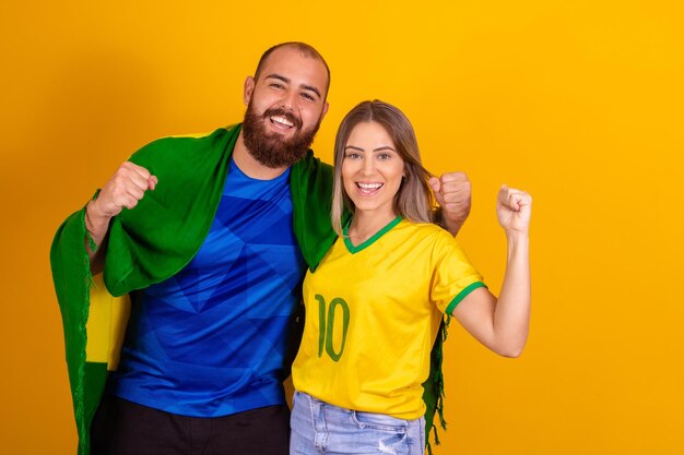 Casal feliz torcendo pelo torcedor do casal brasileiro no fundo amarelo