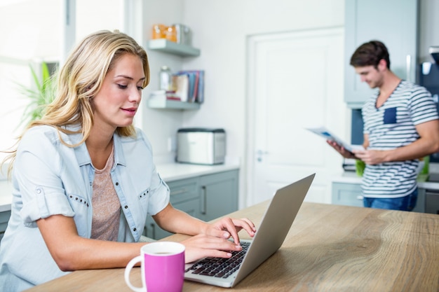 Casal feliz usando laptop e lendo na cozinha