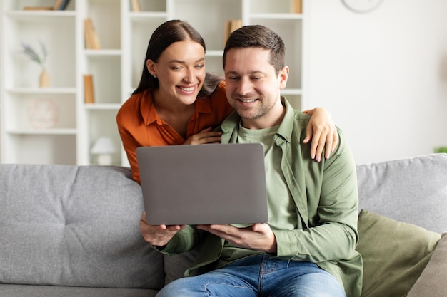 Casal feliz usando laptop fazendo compras on-line ou vendo fotos juntos esposa abraçando marido de