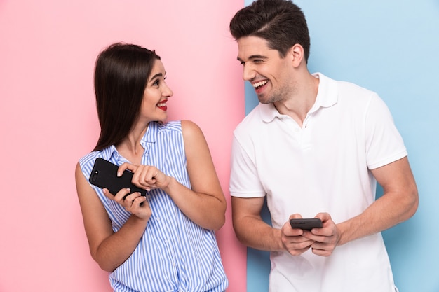 casal feliz usando smartphones juntos, isolados sobre uma parede colorida