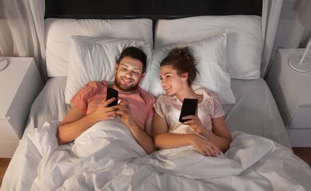 casal feliz usando smartphones na cama à noite