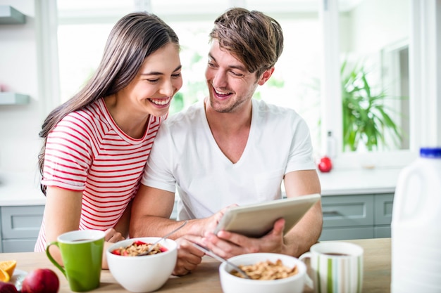 Casal feliz usando tablet e tomando café da manhã na cozinha