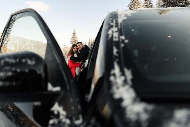 Casal fofo abraçando perto do carro no inverno homem e mulher apaixonada se olham perto do carro