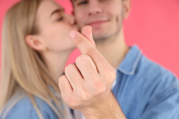 Casal fofo com coração de dedo em fundo rosa