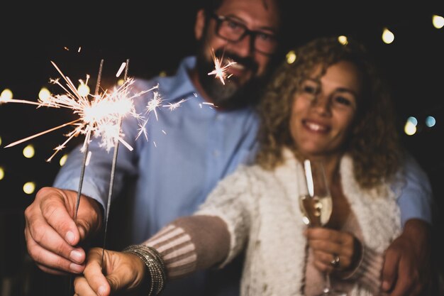 Foto casal fofo de dois adultos apaixonados dando uma derrota juntos na noite de ano novo brincando com estrelinhas na mão perto da câmera