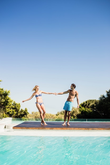 Casal fofo de mãos dadas à beira da piscina