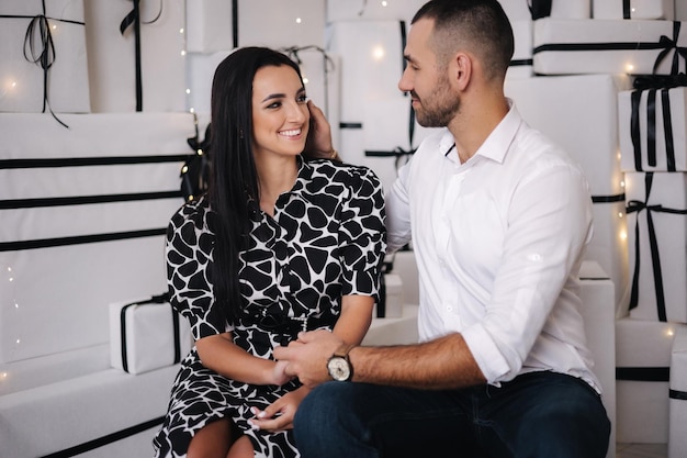 Casal fofo senta-se na frente de uma grande pilha de presentes na época de natal