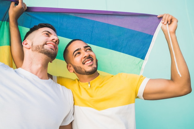 Casal gay abraçando e mostrando seu amor com a bandeira do arco-íris.