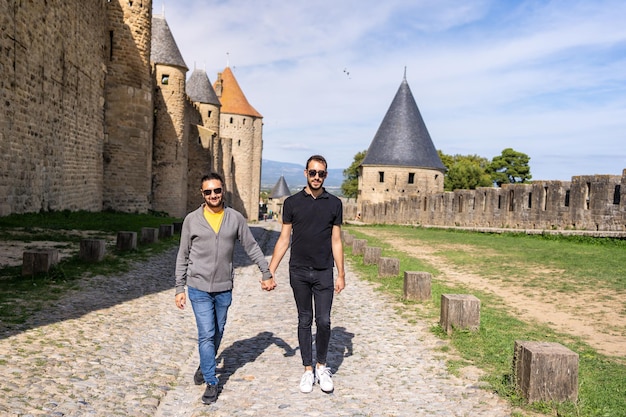 Casal gay andando de mãos dadas ao lado das paredes de um castelo medieval. França