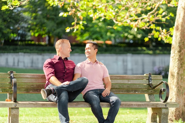 Casal gay apaixonado, homens sentados no banco, abraçados, olhando um para o outro ao ar livre Conceito de amor