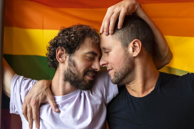 Casal gay apaixonado se beijando com a bandeira lgbtq ao fundo Jovem casal gay se unindo carinhosamente dentro de casa