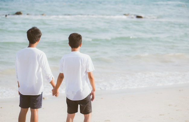 Casal gay asiático juntos de mãos dadas na praia.