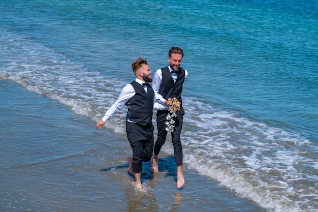 Casal gay casamento Casal gay LGBT tendo um momento romântico juntos Dois homens gays após o casamento em uma praia do mar Conceito de LGBTQ Homens gays andando em uma praia de mãos dadas