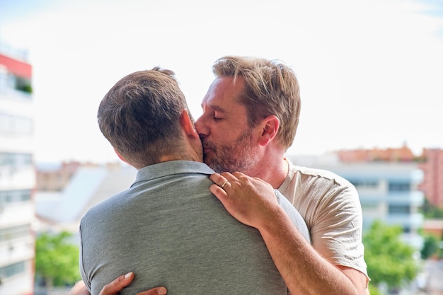 Casal gay de meninos maduros no terraço de seu apartamento abraçando e beijando