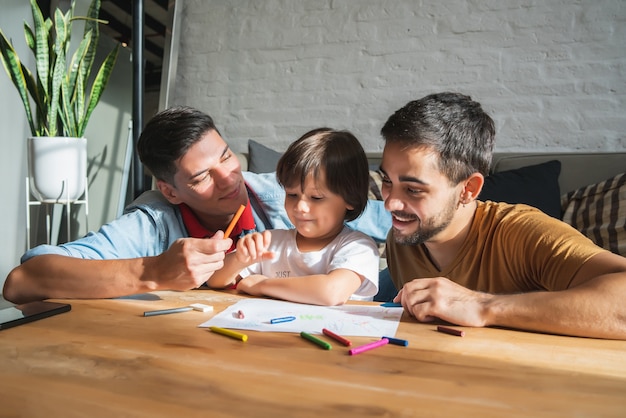 Casal gay e seu filho se divertindo juntos enquanto desenham algo em um papel em casa. conceito de família.