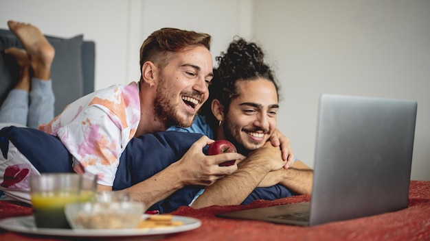 Foto casal gay feliz assistindo filmes no laptop em uma tarde preguiçosa, momento terno e romântico de pessoas lgbt do mesmo sexo