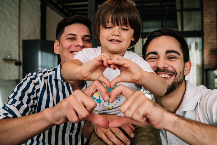 Foto casal gay feliz posando com seu filho ao fazer um formato de coração com as mãos, mostrando amor. conceito de família.